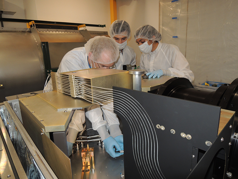 Three instrument team members lean over a large steel box containing the APOGEE South spectrograph