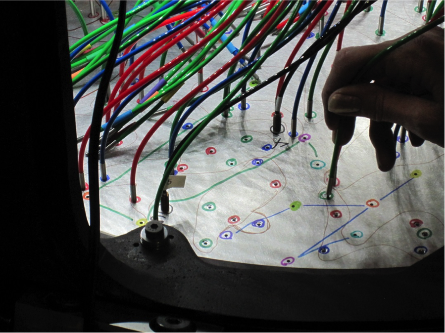 To begin the observation of a plate, fibers are plugged into pre-drilled holes and the fibers then are mapped by shining a laser on the slithead to determine which fibers correspond to which holes (and therefore to which stars). Here, an APOGEE-North fiber is plugged into a plate. Each hole on a plate corresponds to a single object on the sky and the different colored fibers denote faint, medium and bright targets. <em>Photo courtesy of J. Wilson.</em>