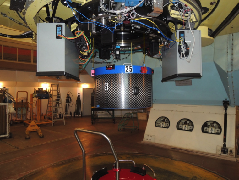 A plugged cartridge is hoisted into place at the Cassegrain focus of the du Pont Telescope using an intricate mounting system. <em>Photo courtesy of J. Wilson.</em>
