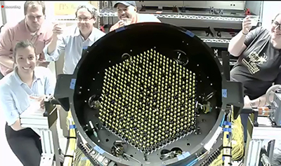 Five people stand next to a hexagon made of fibers on a telescope