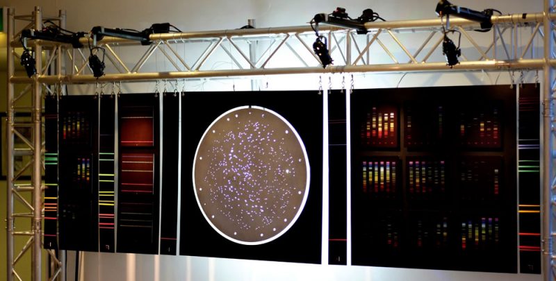 A round SDSS plate with may small holes hanging with rainbow-coloured spectra either side