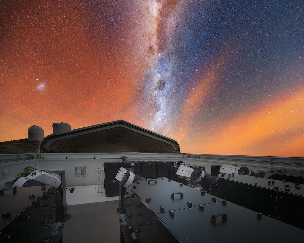 Above the four telescopes of the LVM, the Milky Way appears vertical in the sky with the SMC appearing as a small bright blob to the left.